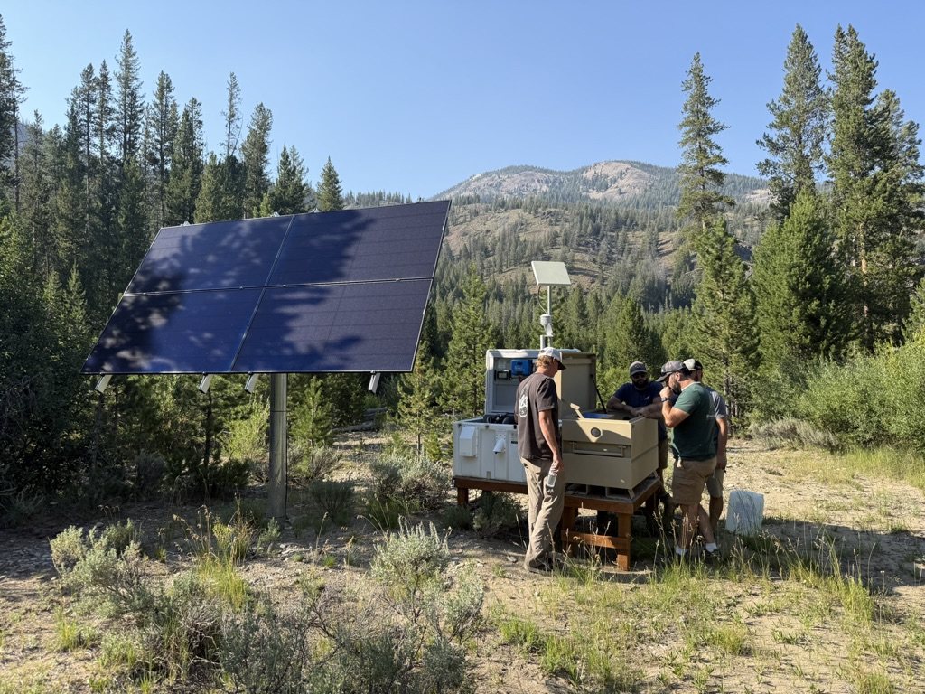 A crew working at a solar-powered equipment enclosure at a remote mountain site