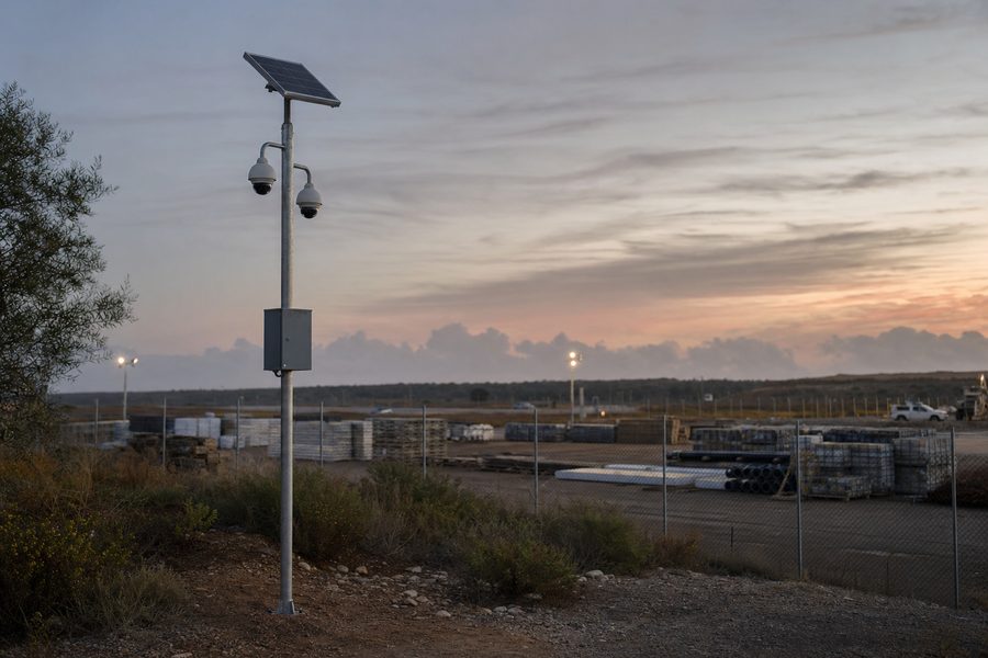 Solar powered pole camera overlooking a fenced industrial yard at dusk